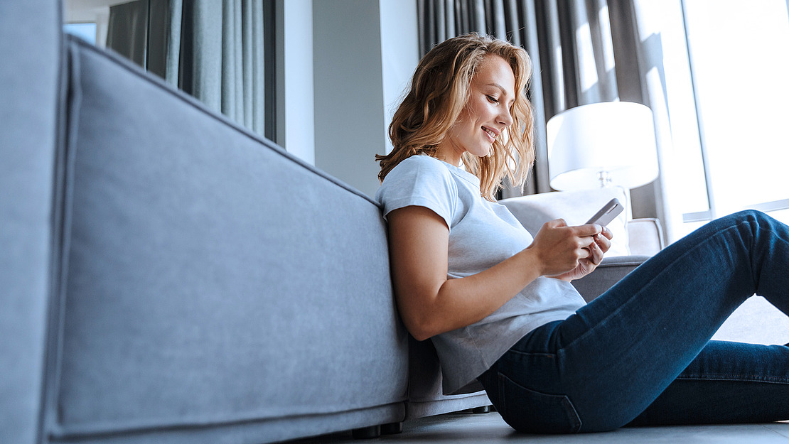 Frau benutzt Smartphone sitzend auf dem Sofa.