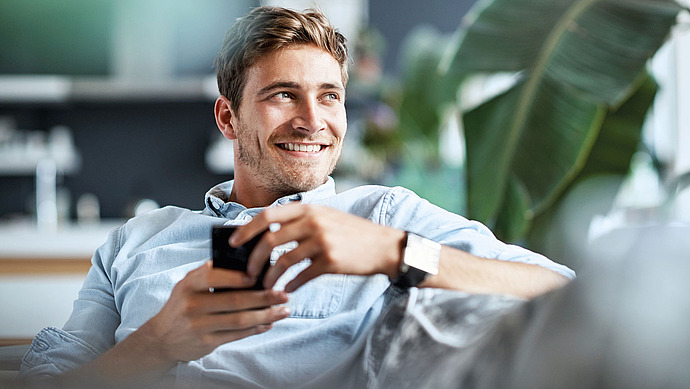 Junger Mann mit Kaffee-Tasse auf einem Sofa