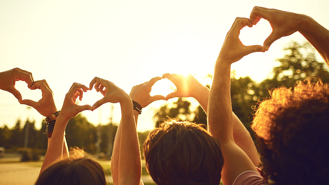 Profitieren Sie von unseren starken Zusatzleistungen Vier Menschen zeigen mit Ihren Händen ein Herzsymbol Richtung Himmel.